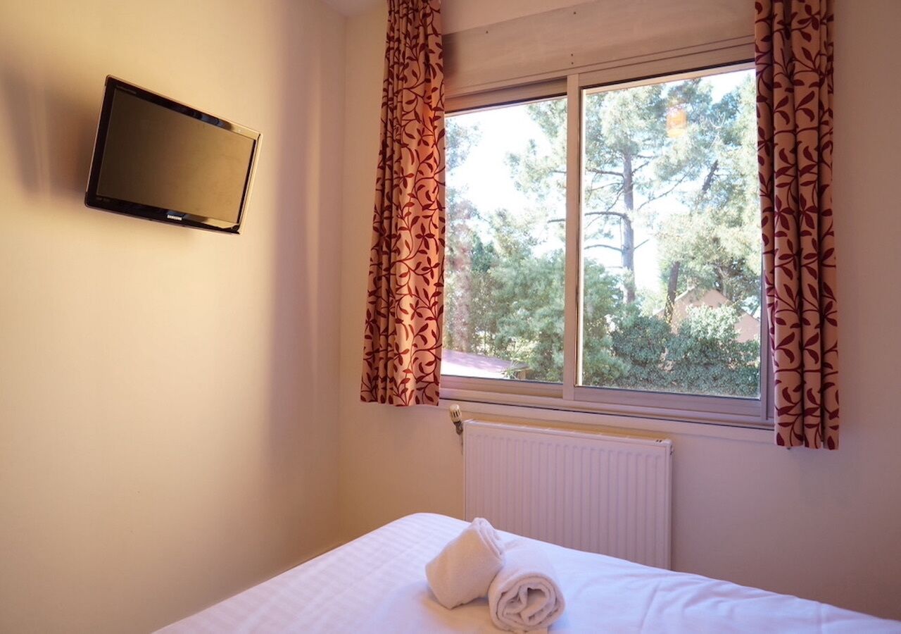 A bedroom with a bed, a TV mounted on the wall, and a window with curtains.