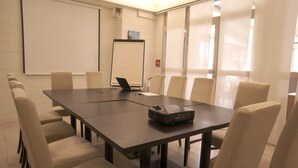 Une salle de conférence équipée d’une grande table, de chaises, d’un projecteur et d’un tableau blanc.