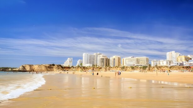 Una platja amb un paisatge urbà al fons, incloent blocs de pisos i penya-segats.