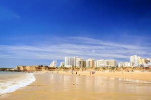 A beach with a cityscape in the background, including high-rise buildings and cliffs. - Casinha da Praia da Rocha – Stunning Sea View (Portimão)