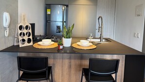 Une cuisine moderne dotée d’un îlot central, de chaises noires, d’une cuisinière encastrée, d’un réfrigérateur et d’un évier avec un robinet au design original.