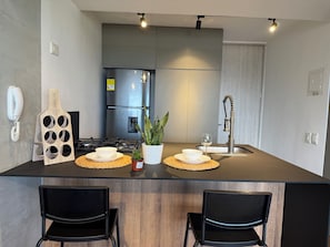 A modern kitchen with a central island, black chairs, a built-in stove, a refrigerator, and a sink with a unique faucet design. - Flora Traveller House (Cali)