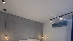 Une chambre moderne avec un grand lit, une petite table de chevet agrémentée d’une plante et un appareil de climatisation fixé au plafond.