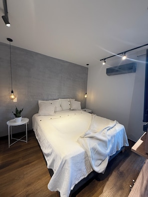 A modern bedroom with a large bed, a small side table with a plant, and a ceiling-mounted air conditioning unit. - Flora Traveller House (Cali)