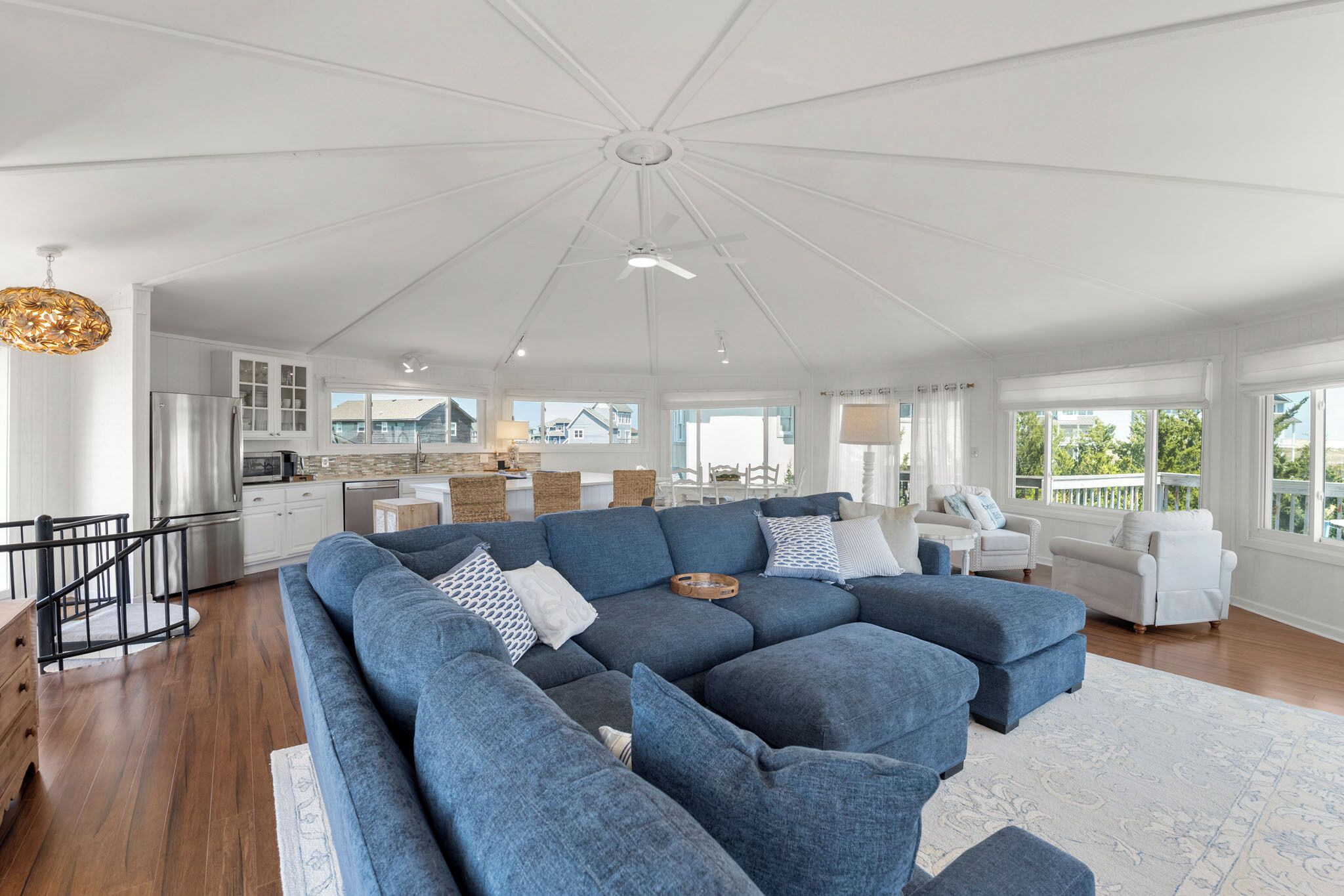 A spacious living room with a large sectional sofa, a kitchen in the background, and a balcony with a railing.
