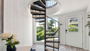 A spiral staircase with a view of greenery outside, a white door, and a vase with flowers on the floor. - Short Walk to Beach | Outdoor Entertainment Area (Salvo)