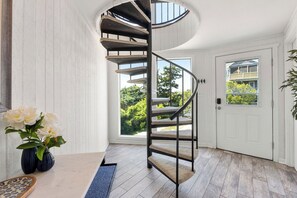 Eine Wendeltreppe mit Blick auf die grüne Umgebung, eine weiße Tür und ein Blumenvasen auf dem Boden.