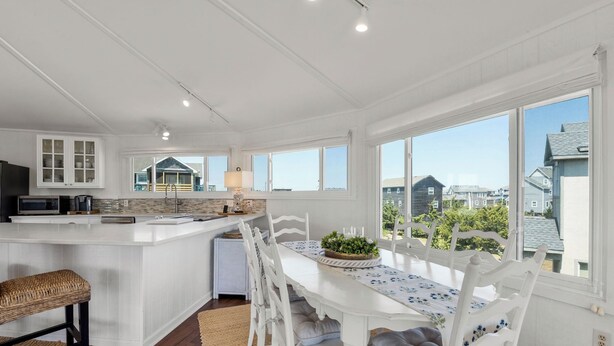 A kitchen with a central island, white cabinetry, and a dining area with a table and chairs. - Short Walk to Beach | Outdoor Entertainment Area (Salvo)