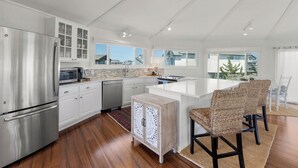 A modern kitchen with white cabinetry, stainless steel appliances, and a large island with seating. - Short Walk to Beach | Outdoor Entertainment Area (Salvo)