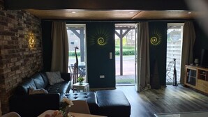 Un salon moderne avec un mur en briques, un canapé en cuir, une petite table surmontée d’un vase, et une vue sur une rue où se trouve une statue de girafe.
