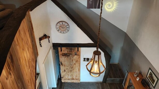 Un escalier en bois avec un intérieur rustique, une porte en bois, une horloge murale et un luminaire suspendu.