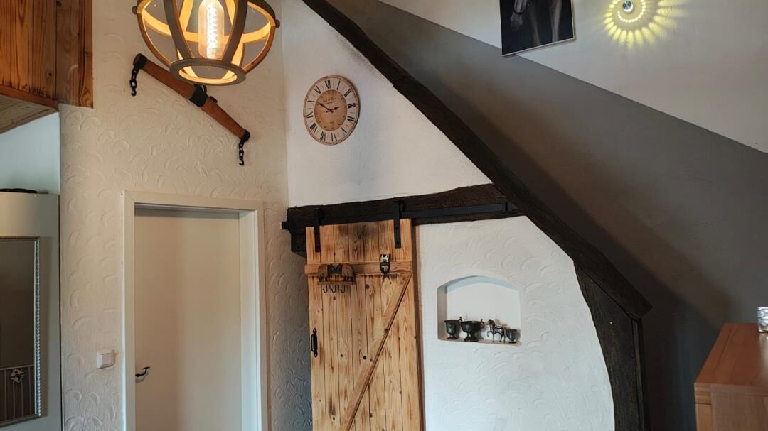 Un intérieur rustique avec une porte en bois, une horloge murale et un luminaire suspendu.