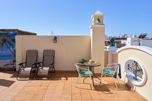 Une terrasse avec deux fauteuils, une petite table et un pot de fleurs.