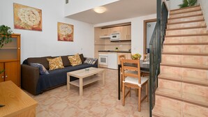 Um espaço compacto com sofá, mesa de centro, mesa de jantar, cozinha e escadas.