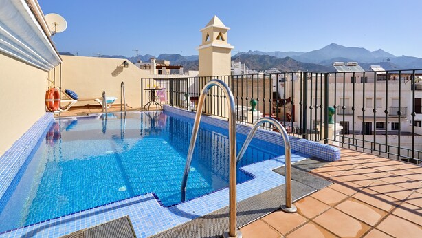 Piscina no terraço com vista clara para montanhas, uma cadeira de salva-vidas e uma pequena estrutura em torre.