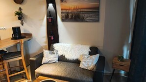 Ein gemütlicher Wohnbereich mit einer Couch, einem Couchtisch, einem Bücherregal und einem Bild von einer Strandlandschaft.