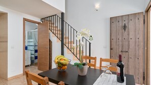 A dining area with a table set for two, a bowl of fruit, a potted plant, and a bottle of wine. - Apartment 'P3 Duplex 2BR for 4-6 Guests' with Pool, Wi-Fi & Air Conditioning (Nerja)