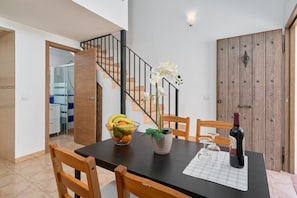 A dining area with a table set for two, a bowl of fruit, a potted plant, and a bottle of wine. - Apartment 'P3 Duplex 2BR for 4-6 Guests' with Pool, Wi-Fi & Air Conditioning (Nerja)