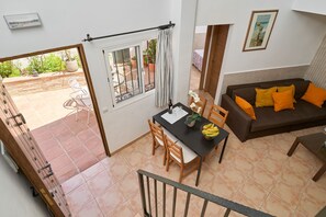 A room with a dining table, chairs, a sofa with orange cushions, a window with curtains, and a view of an outdoor patio. - Apartment 'P3 Duplex 2BR for 4-6 Guests' with Pool, Wi-Fi & Air Conditioning (Nerja)