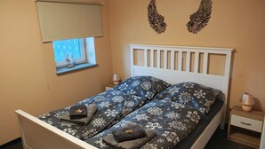 Ein Einzelbett mit weißem Kopfteil, ein kleines Fenster mit Blick und eine Wandlampe.