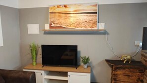 Ein Wohnzimmer mit Flachbildfernseher, einer Holz-Unterhaltungsecke, einem Wandregal mit einem Bild und einer kleinen Pflanze.