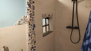 Ein Badezimmer mit Dusche, Fenster und gefliesten Wänden.