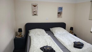 Ein Doppelbett mit gemusterten Betttextilien, zwei Nachttische mit Lampen sowie zwei Wanddekorationen.