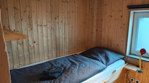 Habitació de fusta petita amb un llit superposat, una finestra que dóna a una vista i una petita taula de nit amb una làmpada.
