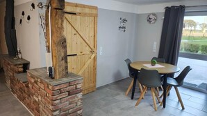 Ein Zimmer mit Kamin aus Ziegelsteinen, einer Holztür, einem runden Tisch mit Stühlen und Blick durch ein Fenster.