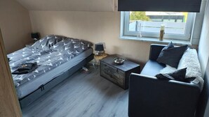Et lille værelse med seng, sofa, et lille bord og et vindue.