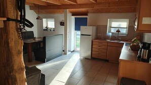 Une cuisine avec des meubles de rangement en bois, un réfrigérateur, un évier et un coin repas comprenant une table et des chaises.
