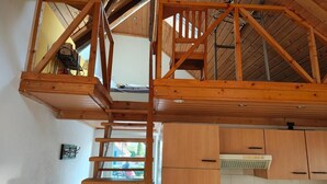 A loft-style room with a wooden staircase, a loft bed, and a kitchenette area. - Modern loft apartment No. 3 with terrace (Aurich)