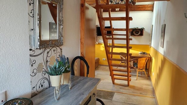 A room with a wooden table, chairs, a ladder, a mirror, and a potted plant. - Modern loft apartment No. 3 with terrace (Aurich)