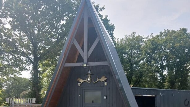 Eine dreieckige Holzhütte mit Tür und einer kleinen Veranda.