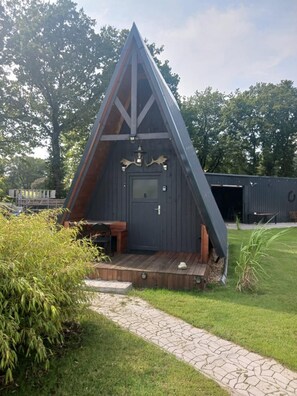 A triangular wooden structure with a door and a small porch. - Ostfriesland hut no. 8 with terrace (Aurich)