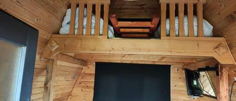 Un interior de madera con balcón, una pantalla negra y una puerta de madera.