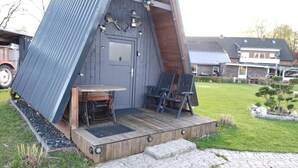 Ein Holzgebäude mit geneigtem Dach, einer Tür und einer kleinen Veranda mit Tisch und Stühlen.