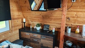 Ein Interieur einer Holzhütte mit an der Wand montiertem Fernseher, einem Holzkabinett mit Schubladen, einer kleinen Pflanze und einer Kreidetafel-Speisekarte.