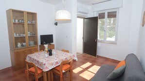Ein Essbereich mit Tisch und Stühlen, einer Speisekammer mit Geschirr, einem Fernseher und einer Couch mit Kissen.