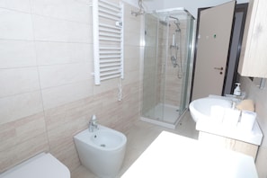 Une salle de bain moderne équipée d’un bidet, d’une douche à parois de verre, d’un lavabo et de toilettes.