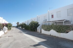A residential street with white houses, a clear sky, and a paved road.