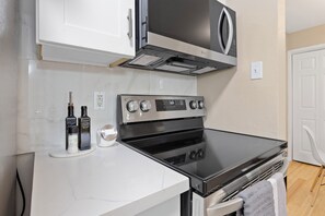 A kitchen with a stainless steel stove, white cabinets, a microwave, and a white countertop.