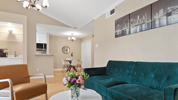 A living room with a teal sofa, a brown armchair, a round coffee table with a vase of flowers, and a cityscape painting on the wall. - 2-bedroom condo in tranquil Greater Uptown, near The Galleria Mall (Houston)