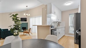 A modern kitchen with white cabinets, a dining area with a round table, and a living room with a sofa and a plant. - 2-bedroom condo in tranquil Greater Uptown, near The Galleria Mall (Houston)