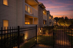 A multi-story building with balconies, a fenced yard, and a sunset sky.