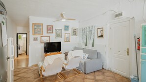 Ein Wohnzimmer mit Fernseher, einer Couch, einem Schaukelstuhl und einem Deckenventilator.