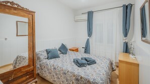 Ein Schlafzimmer mit einem Bett, einem Holzkapuzenpaneel, einem Spiegel, einem Deckenventilator und einem Fenster mit Vorhängen.