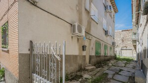Ein schmaler Gang mit einem Gebäude, das ein Metallgitter, Klimaanlagen und eine Steinmauer aufweist.