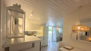 Une cuisine moderne avec des meubles blancs, un coin repas doté d’une table et de chaises blanches, et un plafond avec des poutres apparentes.