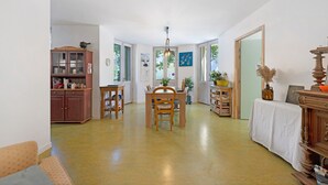A spacious room with a dining table, chairs, a cabinet, and a large window. - Room 1 – Le Toit Vert Inn: Space and Convenience in Moutiers (Moûtiers)